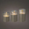 Three lit taper candles in clear glass holders, arranged by size against a dark gray gradient background.