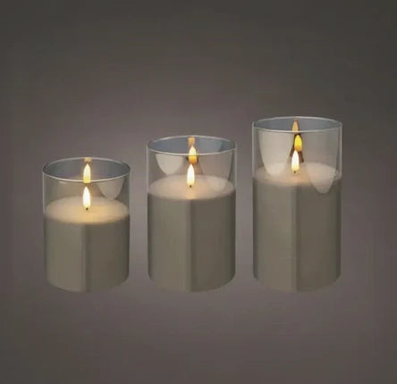 Three lit taper candles in clear glass holders, arranged by size against a dark gray gradient background.