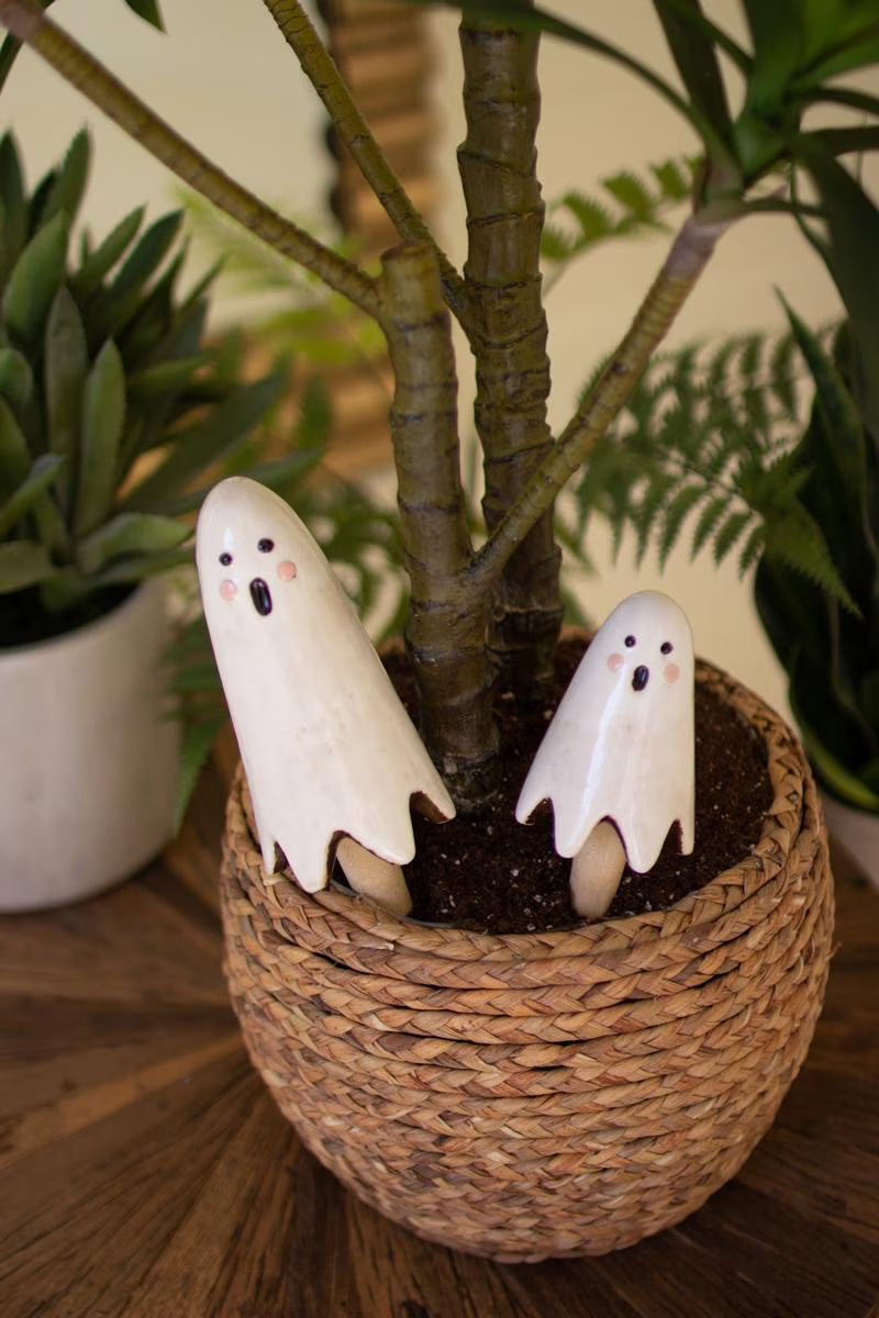 Two white ghost figurines in a woven pot with a plant