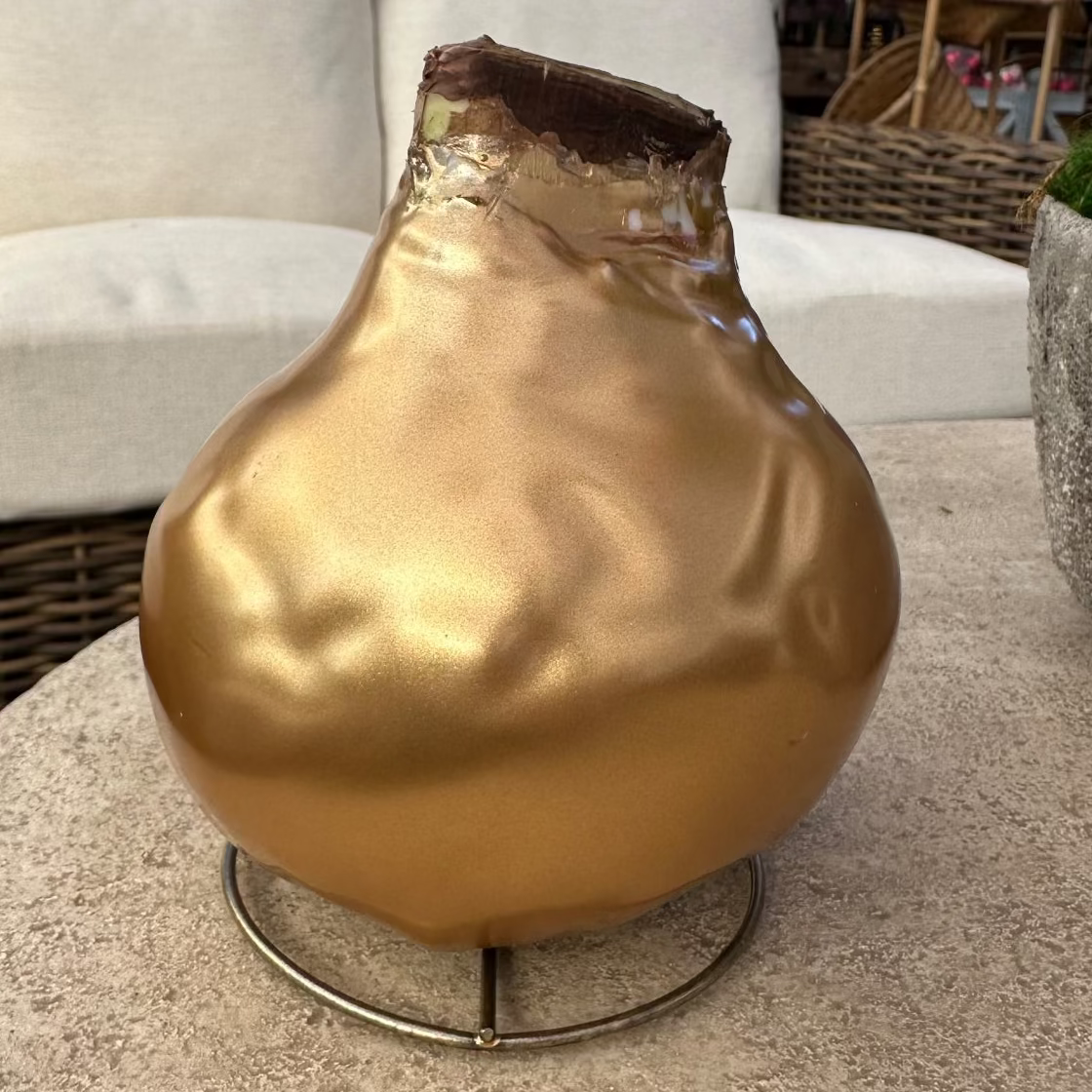 A metallic gold decorative vase with a crumpled foil texture and a dark brown top, displayed on a round stone table in an outdoor patio setting.