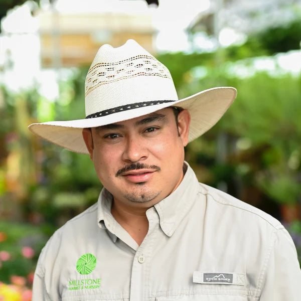 A man wearing a light beige wide-brimmed cowboy hat and a matching light beige button-up shirt with 'MILLSTONE MARINE MFG. CO.