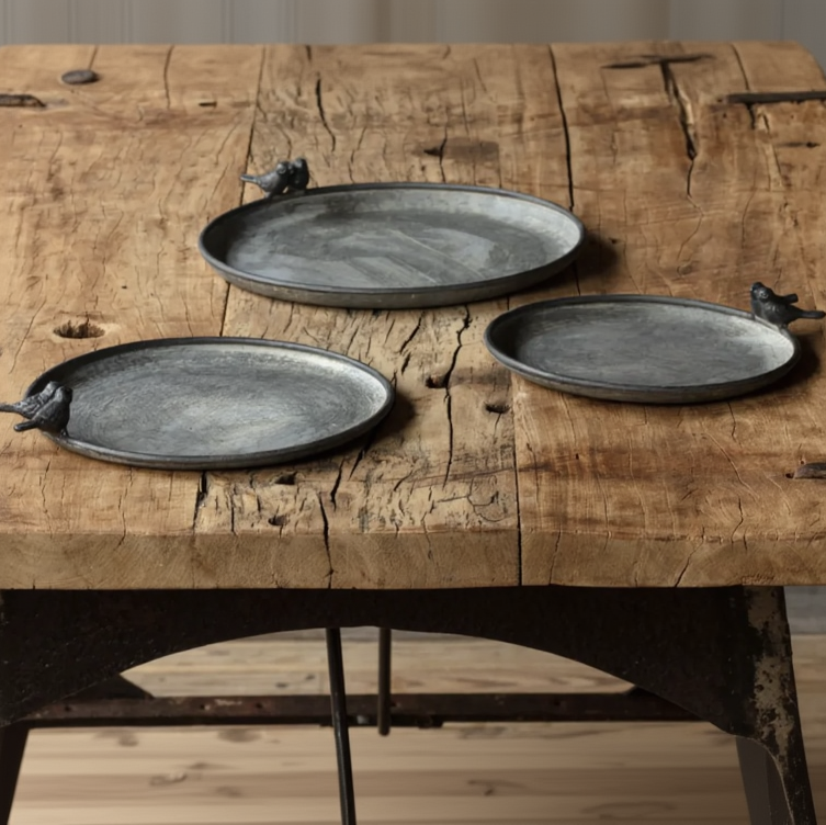 Three round dark gray ceramic plates with bird-shaped handles, displayed on a rustic wooden table.