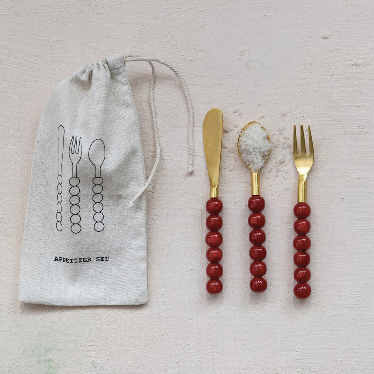 A 3-piece gold and red beaded apptiter set with a matching drawstring bag, displayed on a textured off-white background.