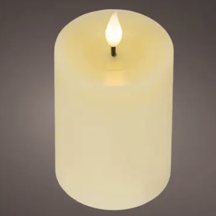 A single lit faux pillar candle with a warm cream-colored body and a glowing flame-shaped bulb on top, centered against a dark gray gradient background.