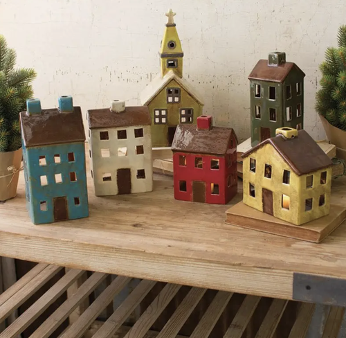 A set of hand-painted wooden house ornaments shaped like a small village, including a church, colorful houses, and a car, displayed on a wooden shelf.