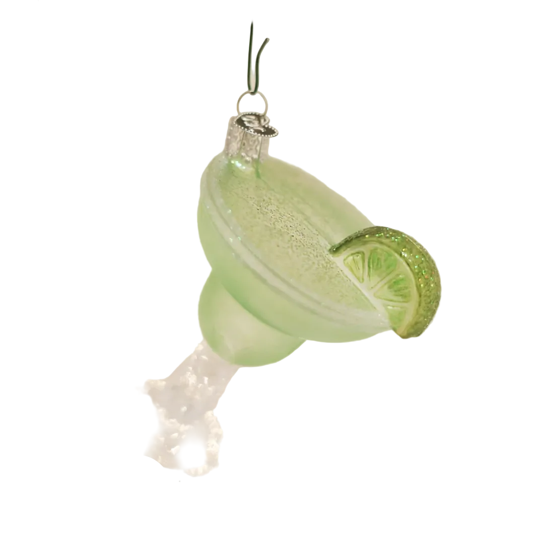 A light green margarita glass Christmas ornament hanging from a tree branch, decorated with a glittery lime wedge garnish, against a soft, blurred holiday background with warm bokeh lights.