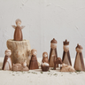 A set of hand-carved wooden nativity figurines arranged on a light surface against a textured off-white wall. The set includes an angel standing on a small tree stump, Mary, Joseph, baby Jesus in a manger, a camel, and three wise men.
