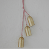 Three small gold bell-shaped hanging ornaments suspended from a red-and-white striped string against a light textured wall.