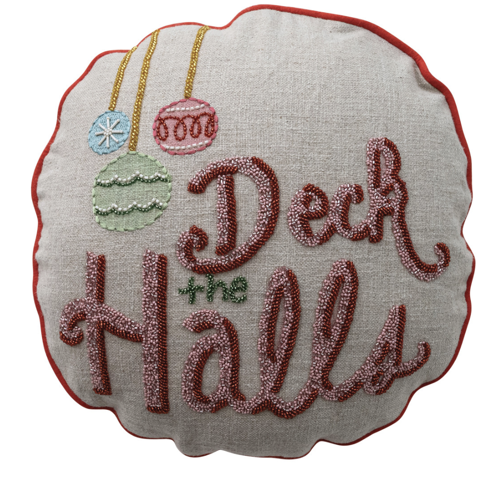 A round decorative throw pillow with scalloped edges, featuring the phrase 'Deck the Halls' in raised pinkish-red embroidered lettering on a light beige linen-like fabric. The pillow is decorated with hanging ornament graphics in blue, green, and pink, outlined with gold embroidery, and finished with a red stitched border.