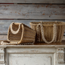 Two woven wicker baskets with thick rope handles, one standing upright and one lying on its side, displayed on a distressed white wooden cabinet against a rustic wood plank wall.