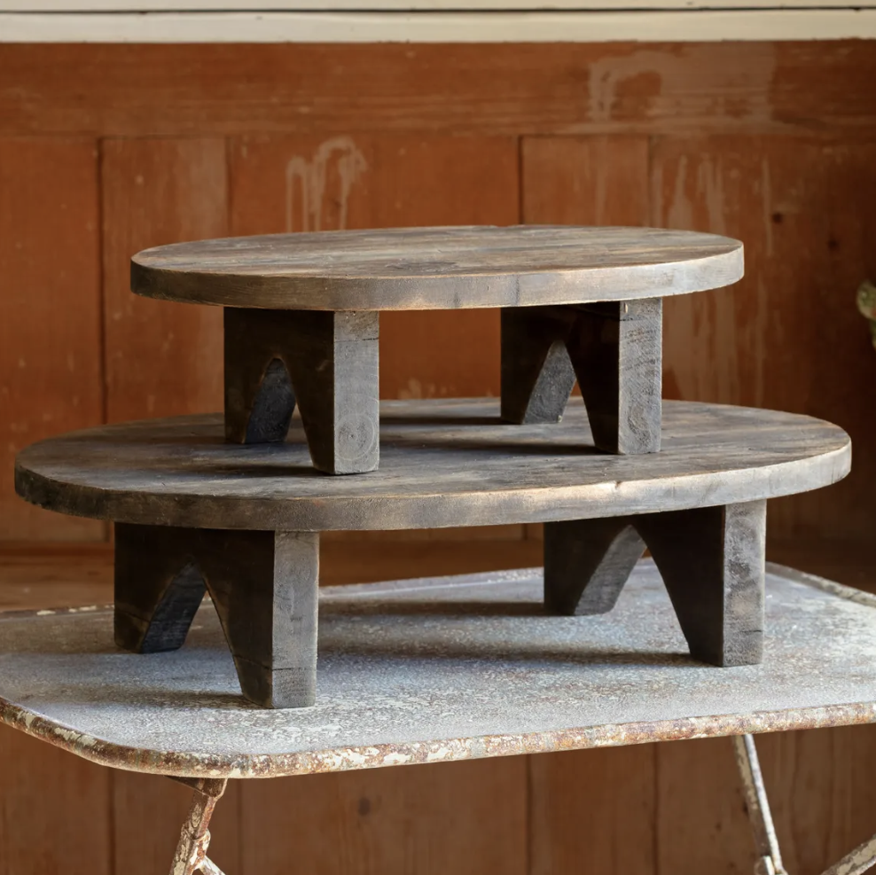 A rustic two-tier wooden coffee table with a dark weathered finish, set on a metal folding table against a warm wood-paneled background.