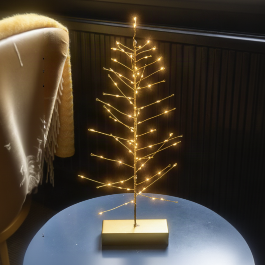 A slim gold wire tree stand decorated with warm glowing fairy lights, set on a rectangular gold base against a dark paneled background.