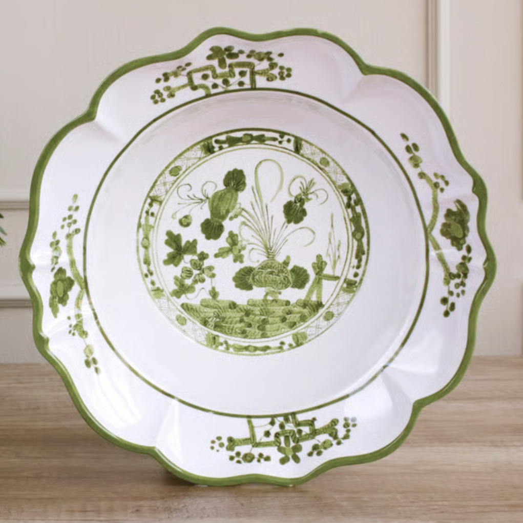 A white ceramic serving platter with a scalloped edge, decorated with a green floral and botanical pattern, displayed on a wooden surface.