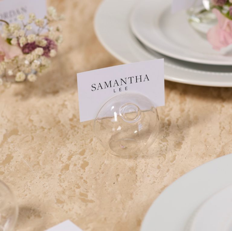 Table setting with place cards and floral decorations on a beige table.