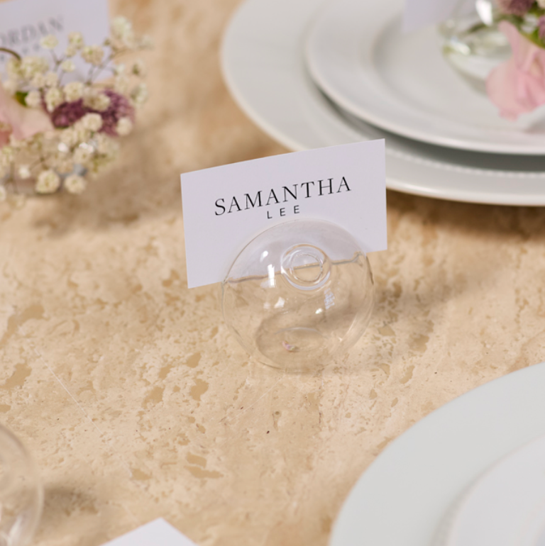 Table setting with place cards and floral decorations on a beige table.
