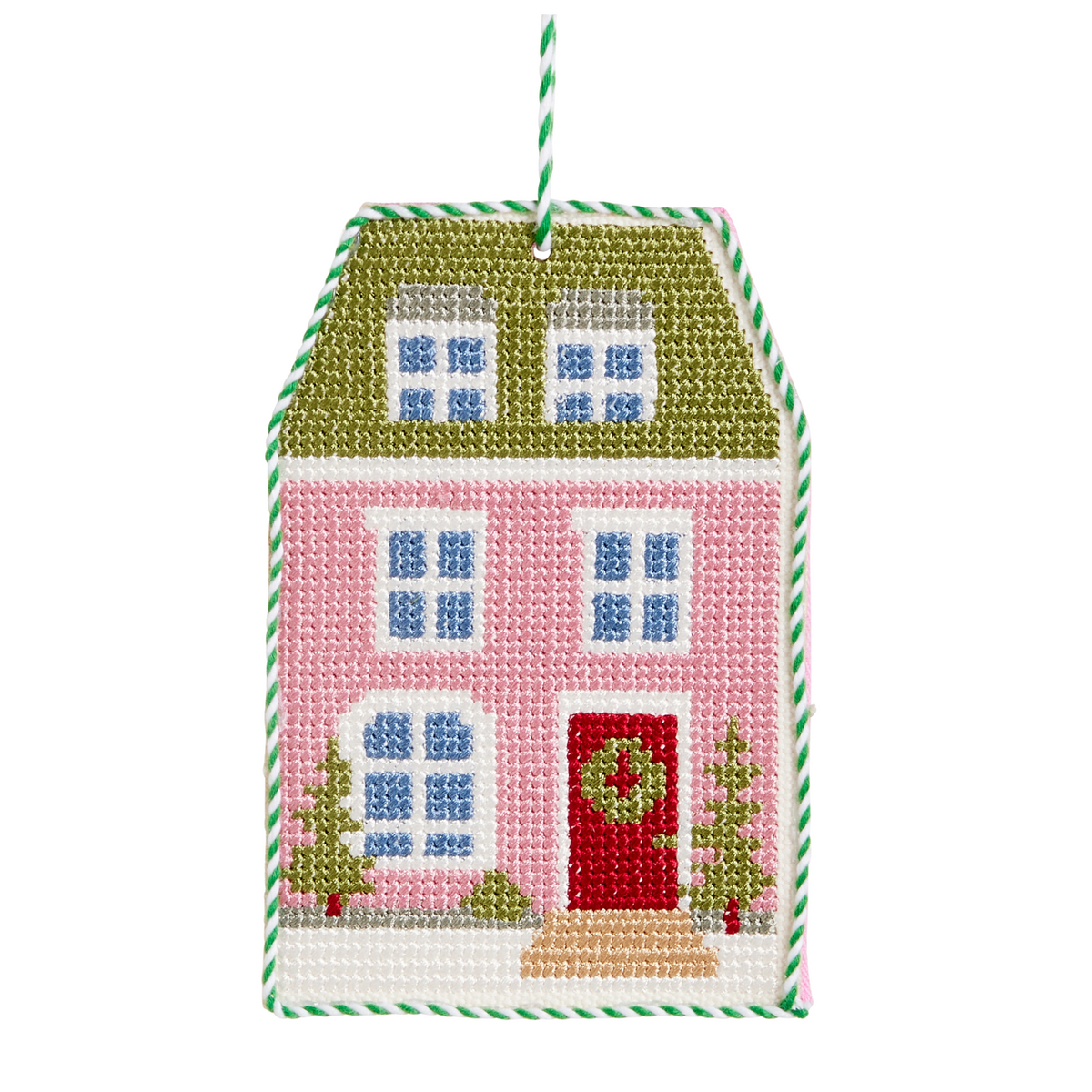 A house-shaped needlepoint ornament featuring a pink facade, green roof, red front door with a green wreath, blue windows, and small green trees, with a green-and-white striped hanging loop.