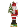 A glittery nutcracker Christmas ornament featuring a Santa-like figure in a red suit holding a small snowy tree, shown on a plain white background.
